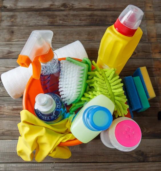 Plastic bucket with cleaning supplies on wood background