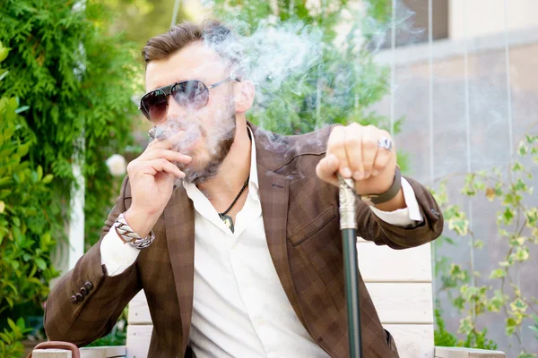 Uomo bello alla moda in abito elegante fumando un sigaro nel parco — Foto Stock