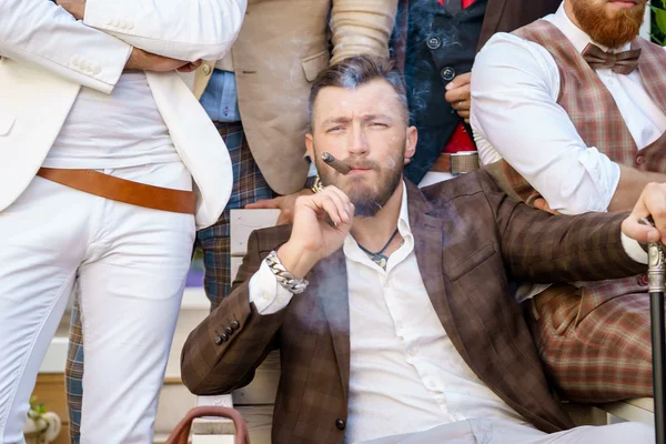 Портрет элегантного стильного успешного мужчины, курящего сигару с друзьями — стоковое фото