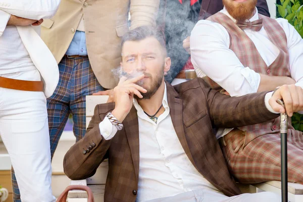 Успешный молодой элегантный мужчина расслабляется с друзьями и курит сигары — стоковое фото