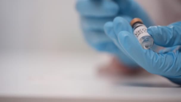 El cierre de las manos del médico en guantes azules de protección llena la vacuna del vial en la jeringa — Vídeo de stock