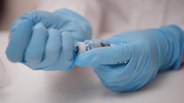 Doktorun ellerini mavi ile kapat koruyucu eldivenler aşıyı şişeden şırıngaya doldurur.