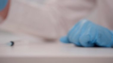 Doktor elleri nitril eldivenlerle masaya bir şişe Covid-19 aşısı koydu.