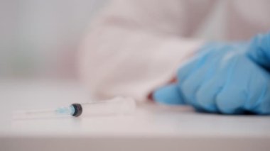 Doktor elleri nitrle eldivenleriyle masaya bir şişe Covid 19 aşısı koydu.