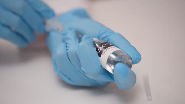 Il contatto ravvicinato delle mani del medico con guanti protettivi blu riempie il vaccino dal flaconcino nella siringa — Video Stock