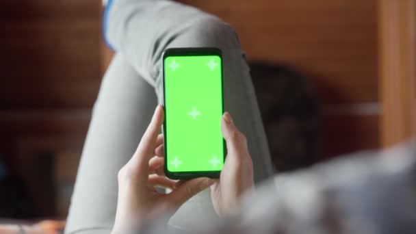 Junge Frau zu Hause lyung und verwenden Smartphone mit grünem Bildschirm. Kamerafahrt aus der Perspektive. — Stockvideo