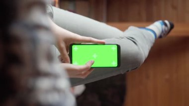 Evdeki genç kadın limonlu ve yeşil ekranlı akıllı telefon kullanıyor. Dikey çekim noktası.
