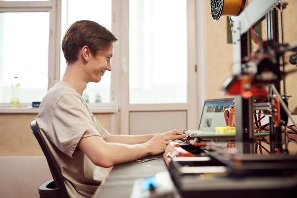 Happy guy using netbook near 3D printers — Stock Photo, Image