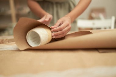 Kırpılmış kadın el işi kağıdına kilden bardak sarıyordu.