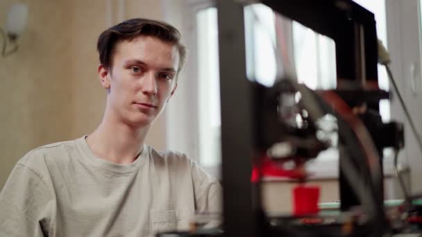 Anak muda duduk di dekat printer 3D yang bekerja — Stok Video