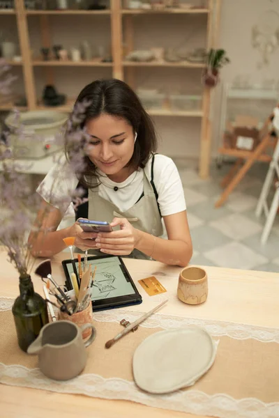 Craftswoman que navega o telefone móvel na bancada — Fotografia de Stock