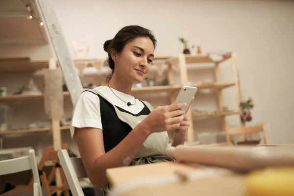 Kobieta rzemieślnik za pomocą telefonu komórkowego w pracowni ceramiki — Zdjęcie stockowe