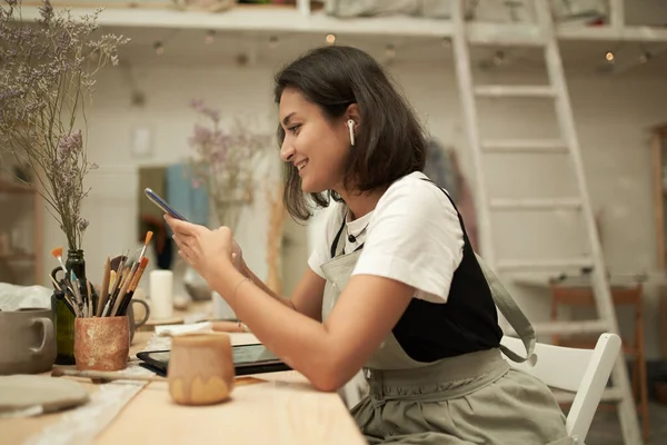 Жінка-художниця використовує мобільний телефон в кераміці — стокове фото
