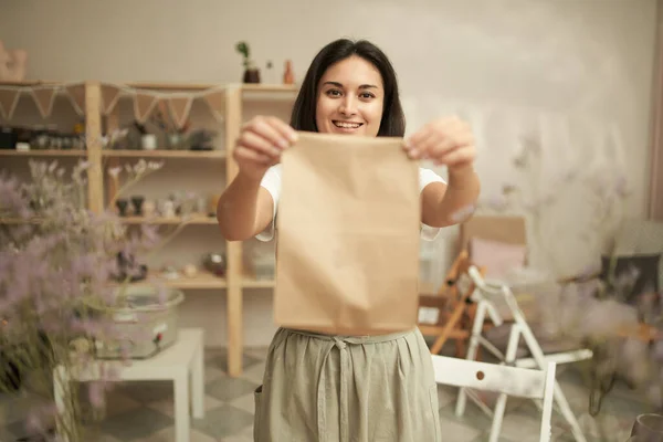 Wesoła kobieta garncarz pokazując papierową torbę — Zdjęcie stockowe
