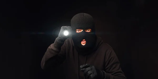 Maskierter Einbrecher mit Taschenlampe auf dunklem Rücken — Stockfoto