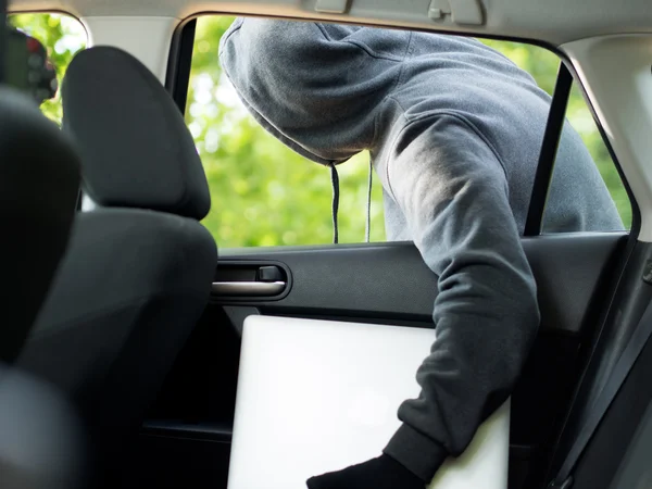 Kradzież samochodu - laptop trwający skradziony przez okno samochodu pustostanów. — Zdjęcie stockowe