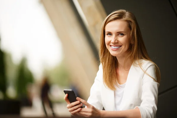 Nő használ egy okos telefon, az utcai kávézóban egy céltalan háttérrel — Stock Fotó