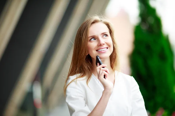 Joven mujer bonita con teléfono móvil. Antecedentes defocus de la ciudad . — Foto de Stock