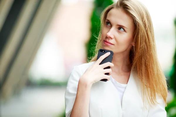 Young pretty woman with mobile phone. City defocusrd background. — Stock Photo, Image