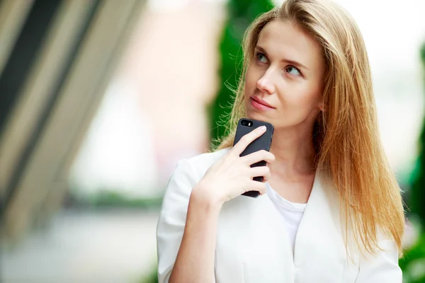 Joven mujer bonita con teléfono móvil. Antecedentes defocus de la ciudad . — Foto de Stock