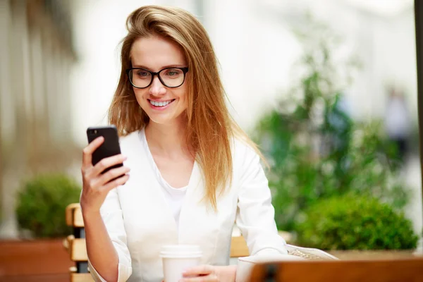 Chica mensajes de texto en el teléfono inteligente en una terraza del restaurante con un fondo desenfocado — Foto de Stock