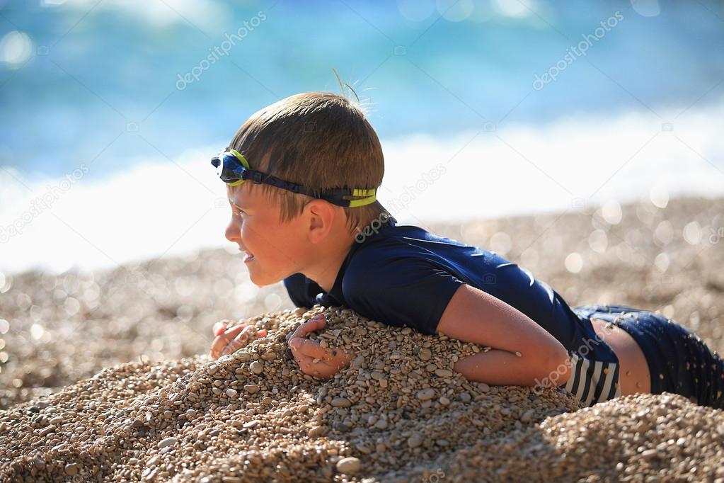 The boy lies on a pebble beach after swimming