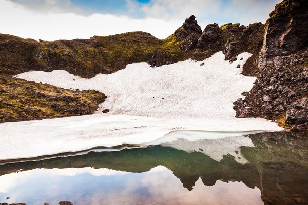 Sin derretir en julio campo de nieve reflejado en el agua — Foto de Stock