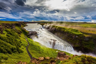 İzlanda 'daki fantastik Altın Şelale Gulfoss. Şelalenin kıyısında turistler için bir patika var. Rüzgarlı bir yaz günü. Ekstrem ve fototürizm kavramı