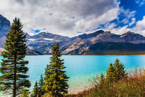 The Majestic Rockies of Canada. The huge Lake Bow is surrounded by cliffs and glaciers. The wind drives lush cumulus clouds over the lake. The concept of active, environmental and photo tourism