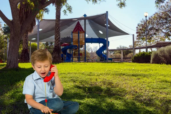 Uroczy Chłopak Rozmawia Przez Czerwony Telefon Przytulny Bezpieczny Plac Zabaw — Zdjęcie stockowe