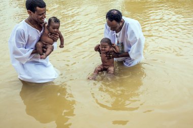 QASR El-YAHUD, ISRAEL - 2 Mart 2020: Bebek Vaftiz Töreni. Beyaz gömlekli iki adam suda durup bebekleri tutuyor. Qasr el-Yahud - Ürdün Nehri üzerindeki İsa Mesih 'in vaftiz yeri. 