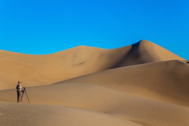 ABD. Mesquite Düz Kum tepeleri, Ölüm Vadisi, Kaliforniya. Kameralı ve tripodlu bir kadın kum tepeleri arasında duruyor. Etkin ve fotoğraf turizmi kavramı