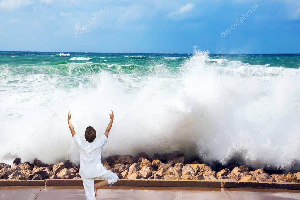  Winter storm in the Mediterranean Sea. Woman performs asana yoga. High foamy surf on Tel Aviv embankment. Concept of eco, active and photo tourism