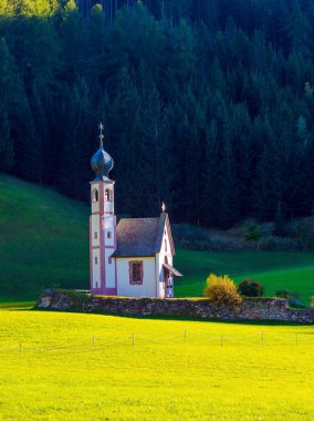 Görkemli Dolomitler. Val di Funes Vadisi. Tyrol, İtalya. Gün batımında yeşil çimlerin arasında çanı olan küçük beyaz bir kilise. Aktif, ekolojik ve fotoğraf turizmi kavramı