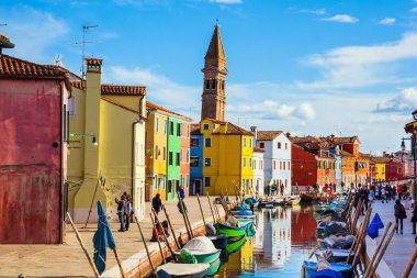 Venedik. Renkli parlak evler ve eğimli bir kule Burano kanallarına yansıyor. Tekneler kanalların kıyıları boyunca park halindedir. Kültür ve fotoğraf turizmi kavramı