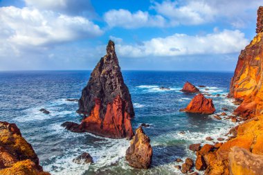 Madeira adasının batı kıyısı - kırmızı kayalar, gök mavisi sörfler. Kör edici gün ortası güneşi kayalık sahili aydınlatıyor. Atlantik 'teki ada. Aktif, ekolojik ve fotoğraf turizmi kavramı
