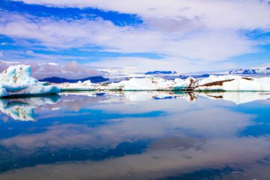 Bulutlar Jokulsaurloun gölünün yumuşak suyuna yansıyor. İzlanda. Soğuk yaz sabahı. Beyaz ve mavi buzdağları ve buz kütleleri soğuk suda yüzer. Kuzey ve fotoğraf turizmi kavramı