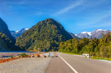 Tarlalar, ormanlar ve tepeler arasında harika bir otoyol. Karlı kaya tepeleri uzaktan görülebilir. Yeni Zelanda 'nın Güney Adası. Harika bir yaz günü. Aktif ve fotoğraf turizmi kavramı