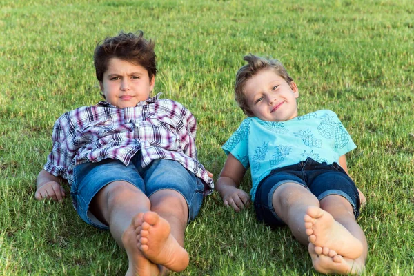 Two boys - brothers are resting on a grassy lawn in a park. Concept - portrait and advertising photography