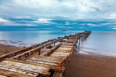 South America. Strait of Magellan. Ruined ocean pier in Punta Arenas. The wooden dock flooring collapsed and rotted. The famous Tierra del Fuego is visible on the horizon.  clipart