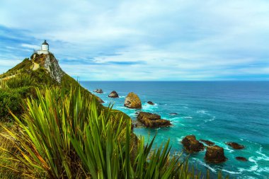 Güney Adası, Yeni Zelanda. Deniz fenerinin beyaz binası yüksek bir pelerin üzerinde muhteşem görünüyor. Nugget Burnu 'ndaki Nugget Point Deniz Feneri. Aktif, çevresel ve fotoğraf turizmi kavramı