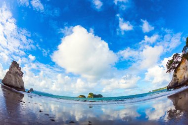 Islak kumdaki bulutların ayna yansımaları. Yeni Zelanda 'nın Kuzey Adası' ndaki Katedral Koyu. Balık gözü lensli fotoğraf. Egzotik, ekolojik ve fotoğraf turizmi kavramı