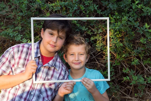 两个可爱的男孩 兄弟们笑着 透过一个白色的框架 绿色夏季公园 肖像和广告照片 — 图库照片