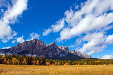 Kanada Kayalıkları 'nda aydınlık bir sonbahar günü. Üç Kız Kardeş Dağı yemyeşil beyaz bulutlarla kaplıdır. Kanada Banff Ulusal Parkı. Aktif, ekolojik ve fotoğraf turizmi kavramı