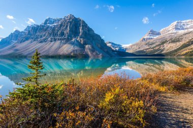 Temiz gök mavisi suyu ile buzul gölü yayı. Dağlar gölün yumuşak suyuna yansıyor. Güneşli bir sonbahar günü. Kanada mı? Rocky Dağları