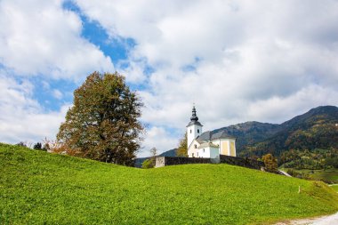  Beyaz kilise ve çan kulesi küçük köyün yakınındaki bir tepede. Dağ vadisinde yeşil çimenler. Slovenya 'ya git. Resimli Julian Alpleri
