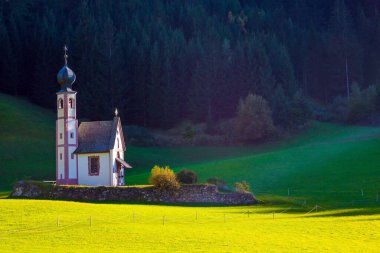 Tyrol, İtalya. Görkemli Dolomitler. Val di Funes Vadisi. Gün batımında yeşil çimlerin arasında çanı olan küçük beyaz bir kilise. Aktif, ekolojik ve fotoğraf turizmi kavramı