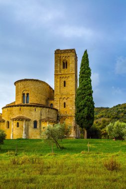 Resimli Toskana usulü. San Antimo 'nun antik ortaçağ muhteşem manastırı. Sonbahar günü. Uzun ince selvi manastırın ön cephesini süslüyor. Aktif, kırsal ve fotoğraf turizmi kavramı