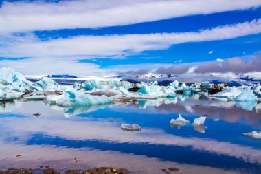 Bulutlar en büyük buzul gölü Jokulsaurloun 'un yumuşak sularına yansıdı. İzlanda. Soğuk yaz sabahı. Beyaz ve mavi buzdağları ve buz kütleleri. Kuzey ve fotoğraf turizmi kavramı