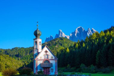 Görkemli Dolomitler. Yeşil vadiyi çevreleyen güçlü dağ zirveleri Val di Funes 'u çevrelemektedir. Gün batımında çanı olan küçük beyaz bir kilise. Tyrol, İtalya. Ekolojik ve fotoğraf turizmi kavramı